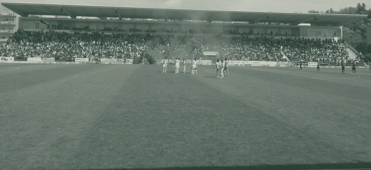 Bancada coberta do Estádio Municipal 25 de Abril em Penafiel cheia de adeptos, com fumo vermelho e jogadores no relvado