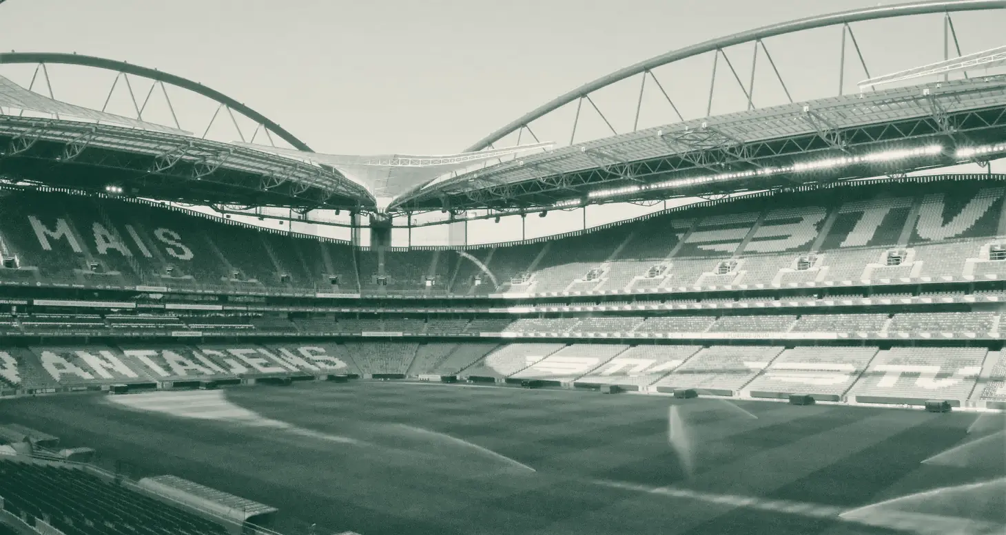Interior vazio do Estádio da Luz com os arcos da cobertura e o relvado a ser regado